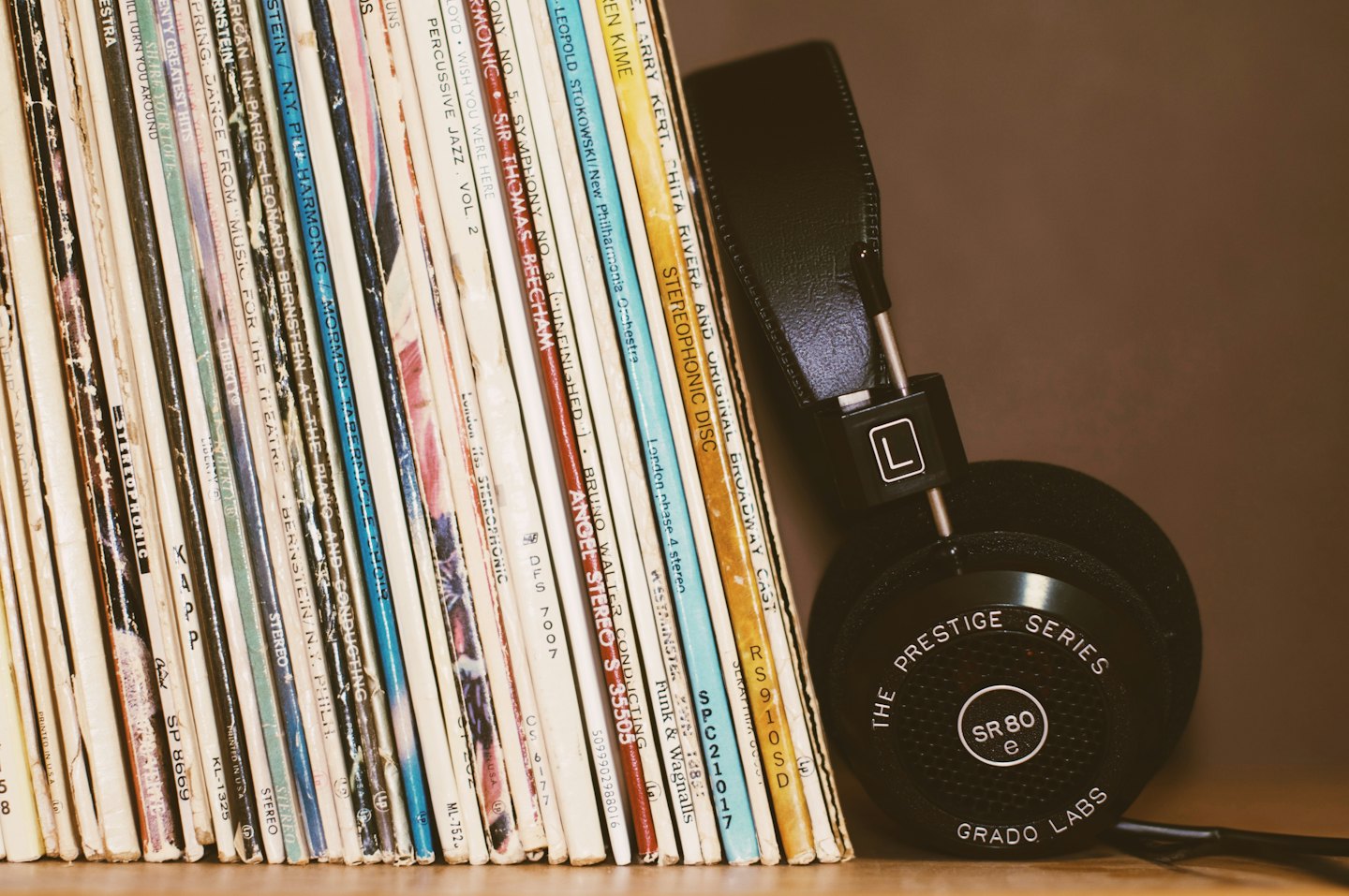 Stack of vintage vinyl records with headphones on a wooden shelf.