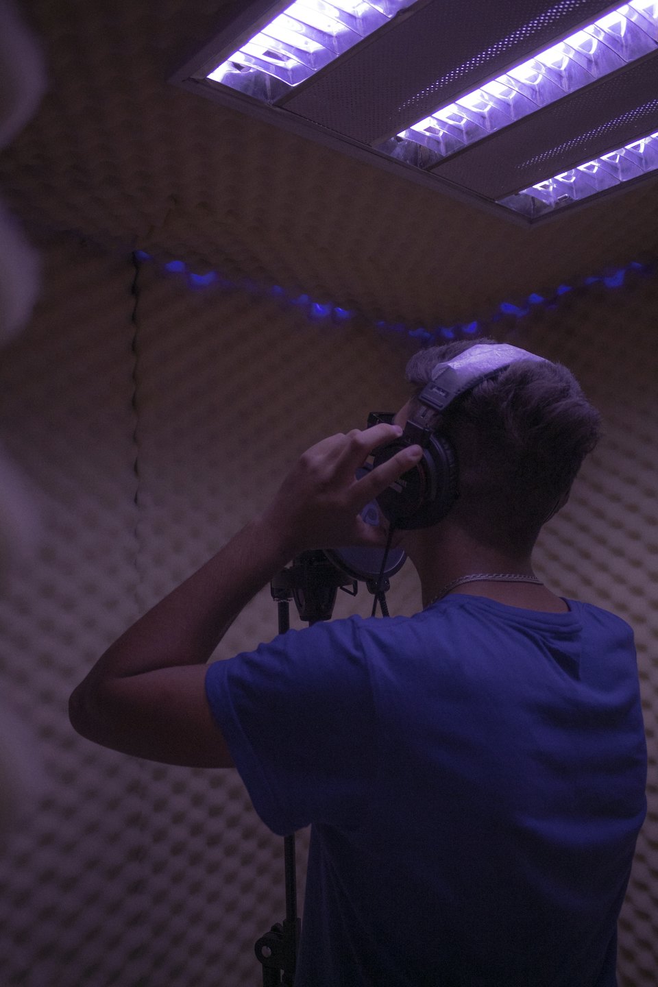 A person wears headphones while recording audio inside an acoustic booth.